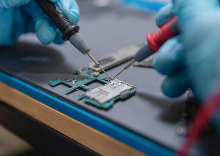 A technician in blue gloves repairing electronic equipment