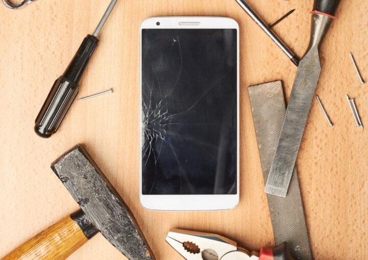 A damaged cell phone with a cracked screen and repair tools scattered around