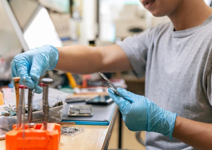 a man in a gray shirt and blue gloves working on a piece of metal