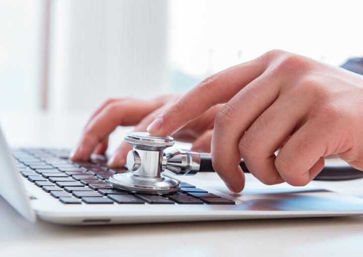 a person typing on a laptop with a stethoscope and a cup of coffee